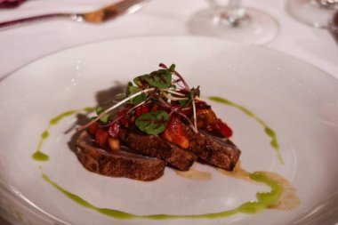 Taze mikroyeşilliklerle kaplı füme ahi balığı dilimleri ve el değmemiş beyaz bir tabak üzerinde fırıl fırıl dönen yeşil bitki soslu kiraz domatesleri.