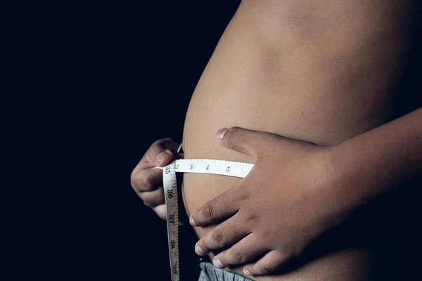 Fat boy holding measuring tape checking the body on black background, take care the health concept.