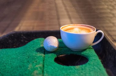 Golf topu yeşil koyarak mat ile sıcak latte kahve Kupası