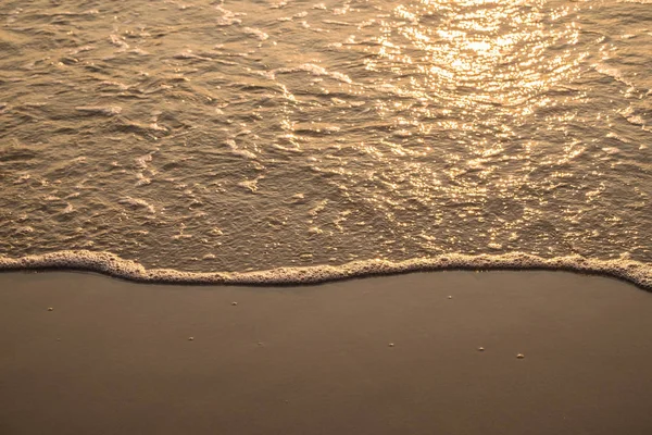 Wave on golden sand in sunrise morning
