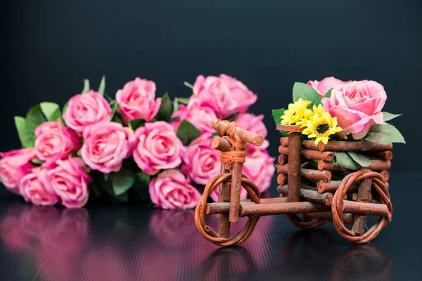 Wooden toy car with bouquet of pink roses on black background