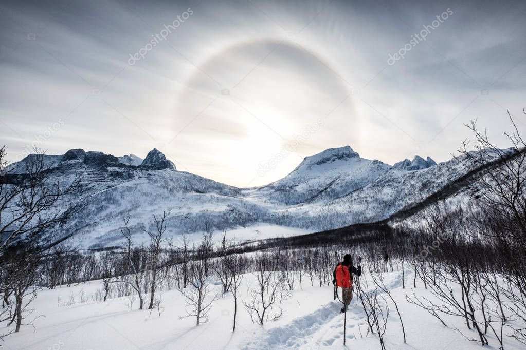 Backpacker climbing on snow peak with Sun halo on mountain range at morning