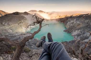 Güneş doğarken ayak krater Kawah Ijen'de zümrüt Gölü ile üzerinde asılı turist. Doğu Java, Endonezya