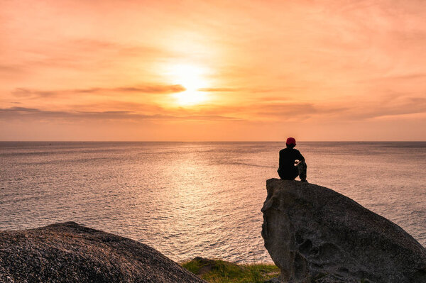 Man sitting on big rock with sightseeing at sunset on sea 