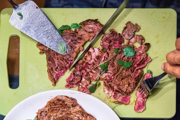 Using knife slicing beef steak on chopped board and fork stabbin