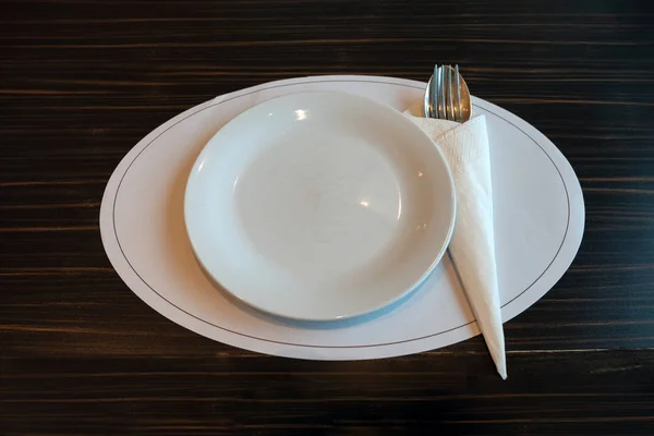 Λευκό κεραμικό πιάτο, κουτάλι, πιρούνι και χαρτοπετσέτας σε ξύλινο τραπέζι — Φωτογραφία Αρχείου