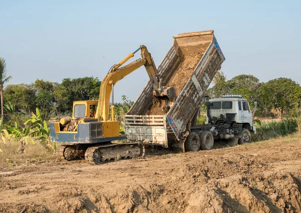 สีเหลือง backhoe ขุดดินเติมในรถบรรทุกด้านหลัง — ภาพถ่ายสต็อก