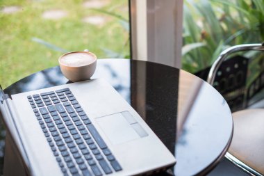 Cam masa üzerinde beyaz fincan sıcak kahve latte ile dizüstü bilgisayar