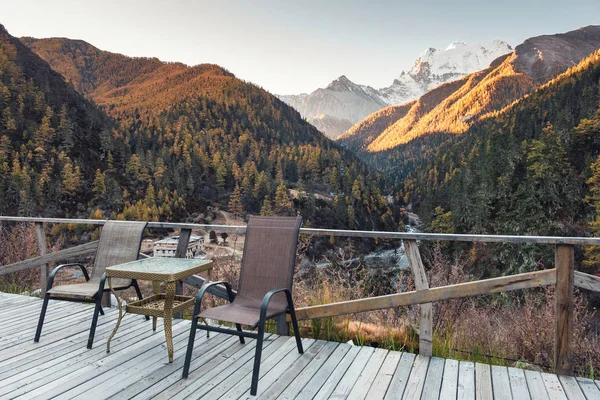 Chairs with table on wooden balcony with valley in autumn at eve
