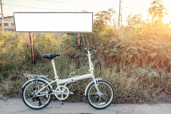 Складывание велосипеда припарковано на лугу с белым постером — стоковое фото