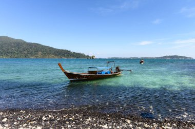Tropikal deniz kıyı şeridinde ahşap tekne ile siyah taş ada