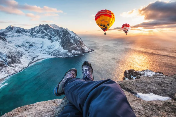 Man hiker cross legs sitting on rock ridge with hot air balloon
