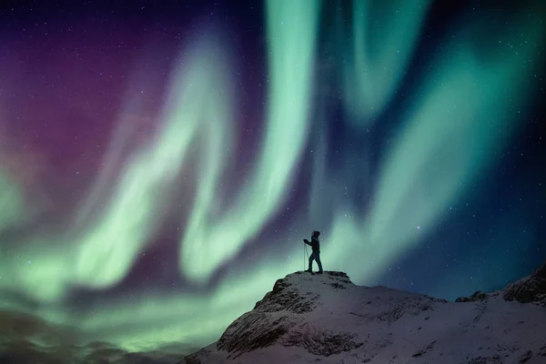 Homem alpinista em pé no pico nevado com aurora boreal e estrela — Fotografia de Stock