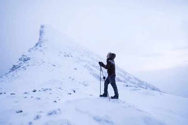 Man klimmer met trekking stokken staande op besneeuwde berg piek — Stockfoto