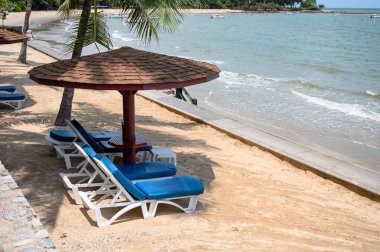 Kumsalda güneşli bir güneş yatağı olan tahta bir şemsiye.