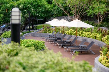 Bahçede havuz kenarında ahşap verandada şemsiye ile şezlong