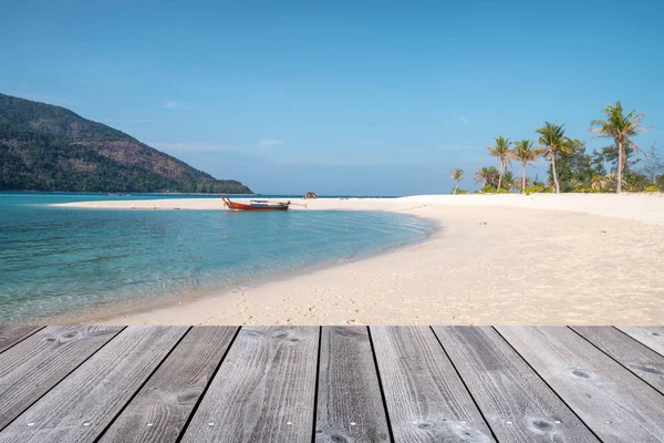 Wooden tabletop on white sand beach with wooden long-tail boat i