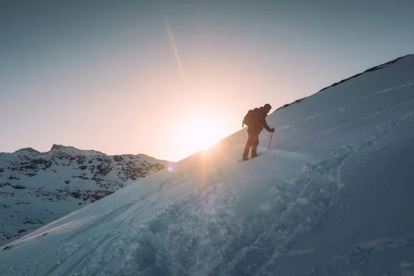 ロフトテン島龍天山の雪の丘と太陽の下でトレッキングポールクライミングを持つ男の登山家 — ストック写真