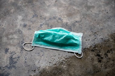 Yeşil tıbbi maske ıslak ve yağmurlu havada beton zemine atılmış.