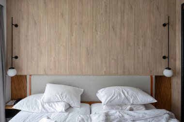 Yatak odası lambasıyla ahşap yatak başlığı, kırışık yastık ve battaniye.