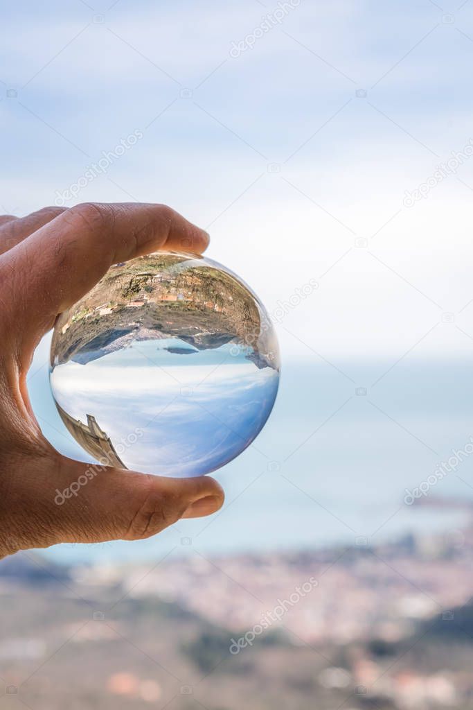 Popular summer resort town Budva on the Adriatic coast in Montenegro reflected in a transparent round sphere ball held by a caucasian man