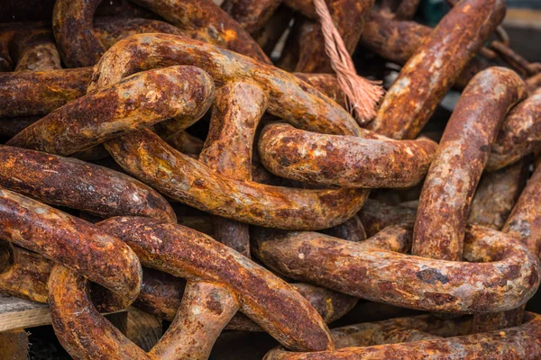 Pile of old, large and heavy rusty chain links in a marina landing in fishing port