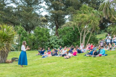 Marazion, İngiltere - Mayıs 2018: bir çim üzerinde oturan turist ve battaniye St Michael Mount kale bahçeleri tepe üzerinde ve kadınla öyküleri ve halk efsaneleri, Cornwall, İngiltere'de dinleme