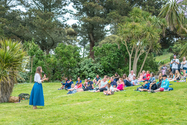 Маразион, Англия - май 2018 года: Туристы, сидящие на траве и одеялах на склоне холма в саду крепости Св. Михаила Маунта и слушающие рассказы женщин и народные легенды, Корнуолл, Великобритания
