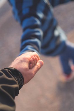 Küçük çocuk babasıyla birlikte yürüyor ve elini tutuyor.