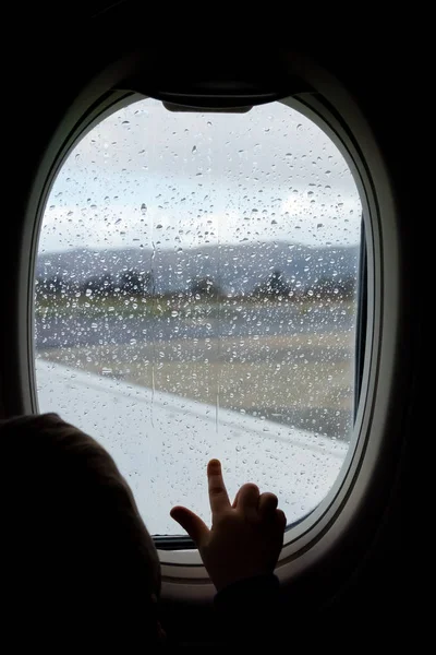 Little boy looking through the plane window before take off in the rain