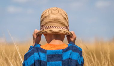 Hasır şapka duran sarı çim sahası önünde giyen küçük çocuk