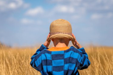 Hasır şapka duran sarı çim sahası önünde giyen küçük çocuk