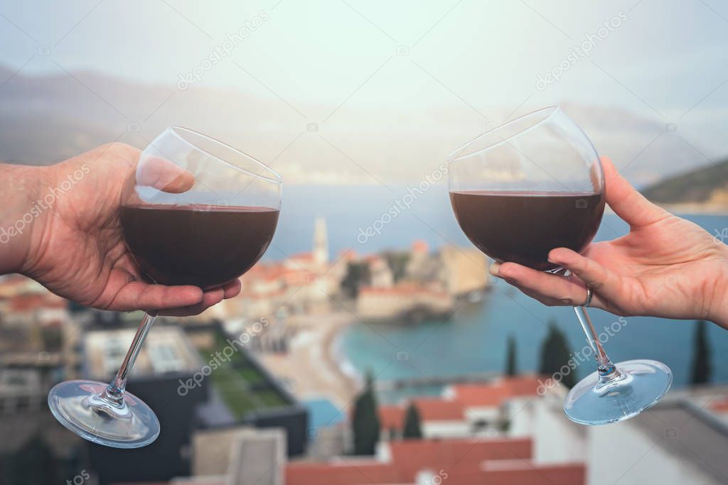 Man and woman holding glasses with red wine on the balcony of their apartment in the Budva town, Montenegro