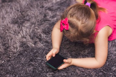 Halı evde bir odada yatan ise bir smartphone cep telefonu ile çizgi film izlerken küçük kız