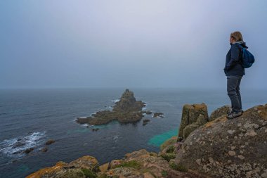Yalnız turist bir uçurumun üstünde duran ve kayalık oluşumlar Lands End üzerinde-en batı noktası İngiltere, popüler turistik, Penwith Yarımadası, Cornwall hayran su geçirmez ceket