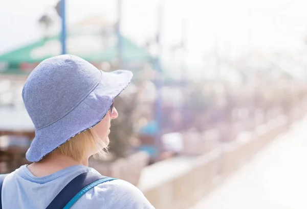 在避暑度假胜地的海滨小镇上 带着一顶蓝色帽子走在阳光明媚的海滨长廊上的白人妇女 — 图库照片