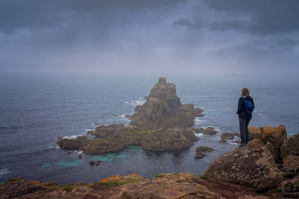 Yalnız turist bir uçurumun üstünde duran ve kayalık oluşumlar Lands End üzerinde-en batı noktası İngiltere, popüler turistik, Penwith Yarımadası, Cornwall hayran su geçirmez ceket
