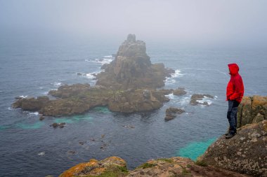 Yalnız turist bir uçurumun üstünde duran ve kayalık oluşumlar Lands End üzerinde-en batı noktası İngiltere, popüler turistik, Penwith Yarımadası, Penzance, Cornwall hayran su geçirmez ceket
