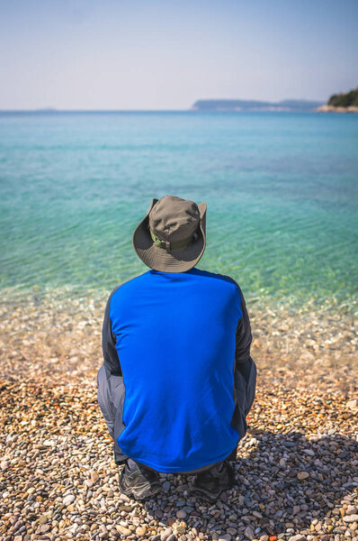 Tourist wearing a hat standing on a beach and looking at the stunning Croatian coast in Dubrovnik