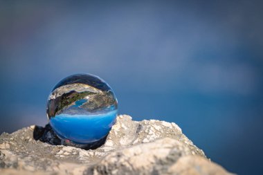 Stunning landscape of the Bay of Kotor and Lovcen National Park in Montenegro reflected in a large glass ball placed on a large boulder clipart