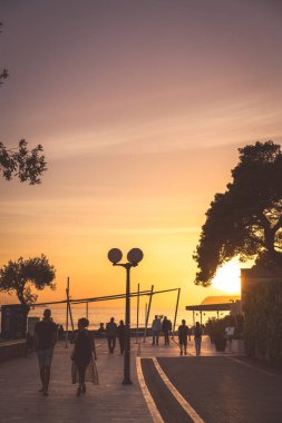Dubrovnik, Hırvatistan - Nisan 2018: Dubrovnik Lapad banliyösünde günbatımında bir deniz kıyısında yürüyen insanlar gezi