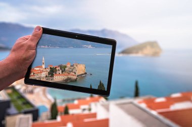 Budva 'nın Budva kentindeki dairesinin balkonunda dururken elinde Budva resmi olan bir tablet tutan adam.