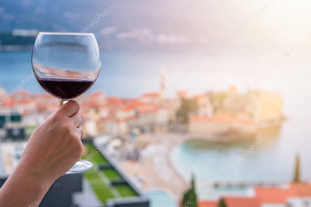 Woman holding glass with red wine on the balcony of her apartment in the Budva town, Montenegro