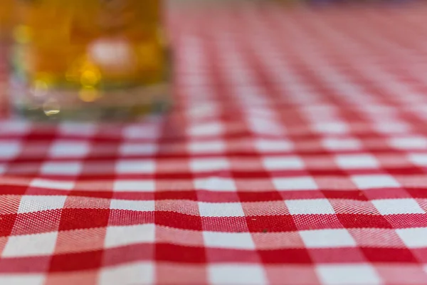 Copo desfocado de cerveja em uma toalha de mesa chequered — Fotografia de Stock