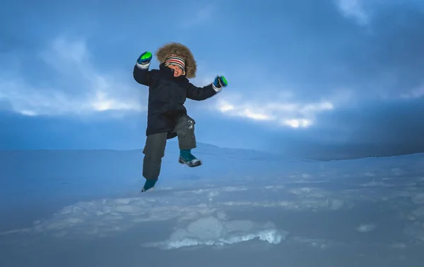 Lycklig liten pojke hoppar i snön — Stockfoto