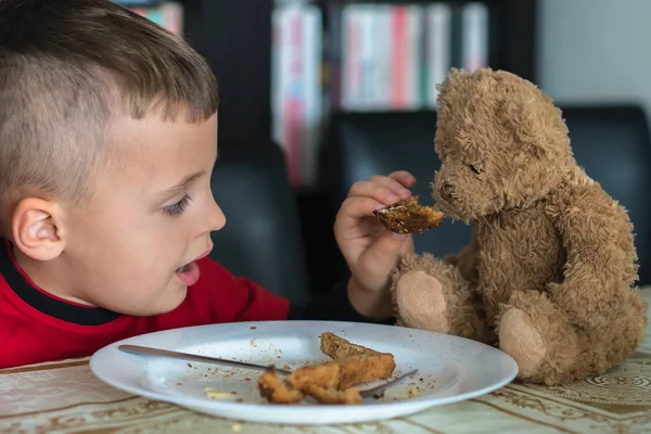 Küçük çocuk oyuncak ayısıyla kahvaltı yapıyor. — Stok fotoğraf