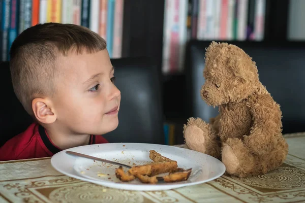 Küçük çocuk oyuncak ayısıyla kahvaltı yapıyor. — Stok fotoğraf