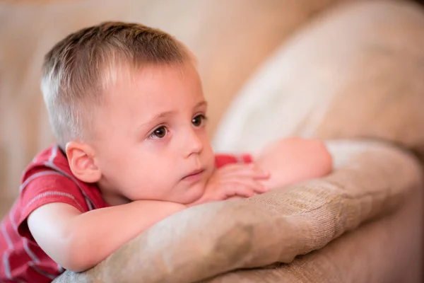 Bonito menino sentado em um sofá e assistindo TV — Fotografia de Stock