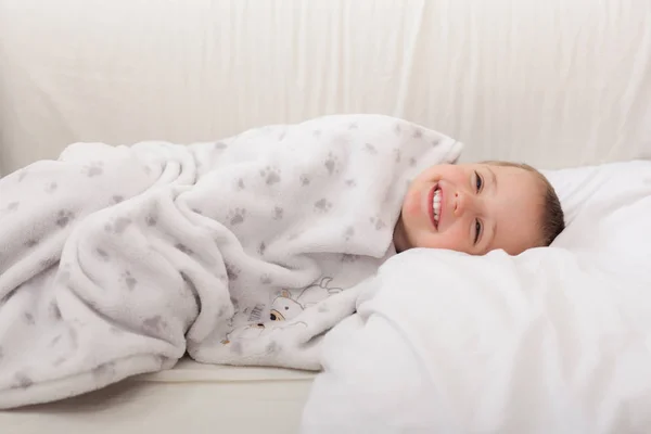 Rapaz bonito embrulhado sob grande cobertor — Fotografia de Stock