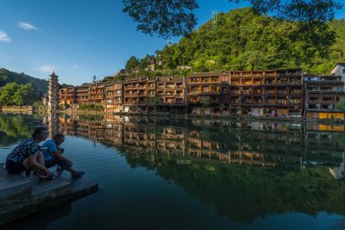 Feng Huang, Çin - Ağustos 2019: Feng Huang Eski Huang Kasabası 'ndaki tarihi Fenghuang Wanming Pagoda Kulesi manzaralı merdivenlerde oturan insanlar